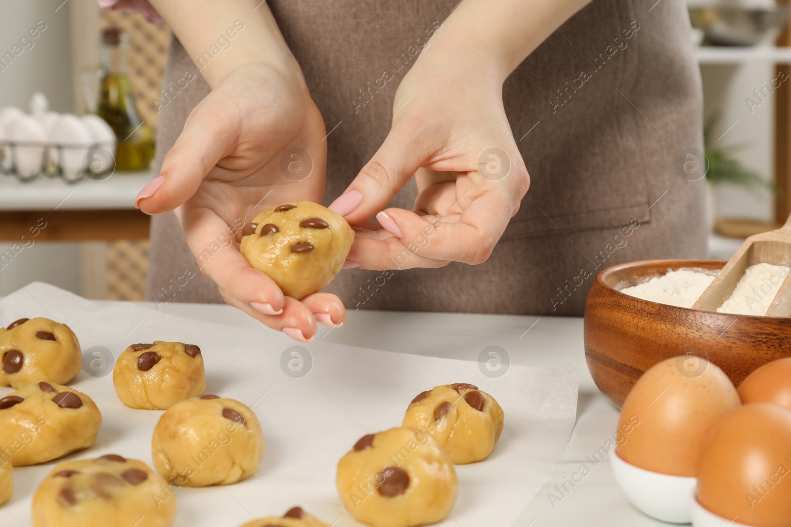 Photo of Woman preparing chocolate chip cookies at white table in kitchen, closeup