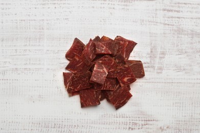Photo of Delicious beef jerky on white wooden table, top view