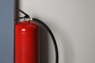 Photo of Fire extinguisher near light wall indoors, closeup. Space for text