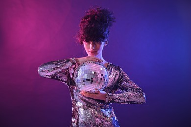 Photo of Beautiful young woman with disco ball posing on color background in neon lights