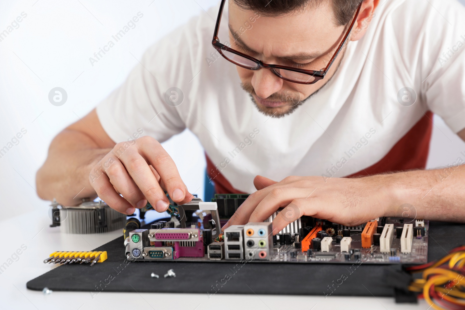 Photo of Male technician repairing motherboard at table against light background