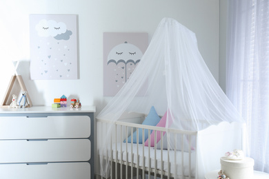 Photo of Baby room interior with cute posters, chest of drawers and comfortable crib