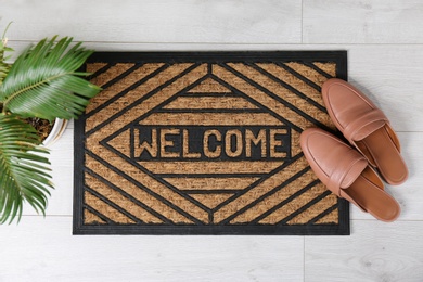 Photo of Door mat with word WELCOME and shoes on floor, top view