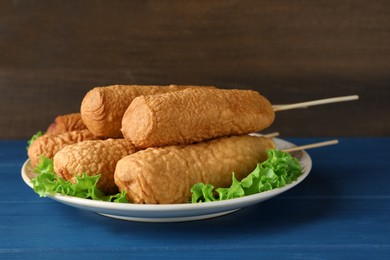 Photo of Delicious deep fried corn dogs with lettuce leaves on blue wooden table