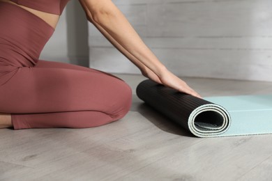 Woman rolling yoga mat on floor indoors, closeup