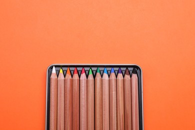 Photo of Box with many colorful pastel pencils on orange background, top view and space for text. Drawing supplies
