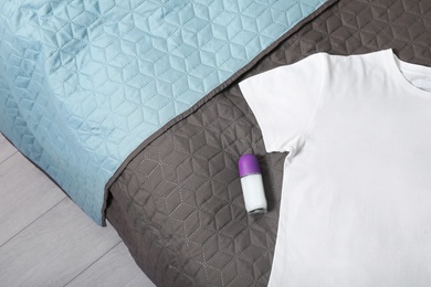 Photo of Female roll-on deodorant and white t-shirt on bed, top view. Space for text