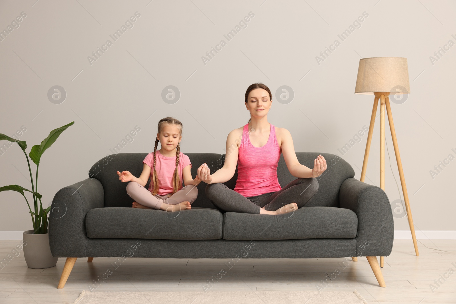 Photo of Mother with daughter meditating on sofa at home. Harmony and zen