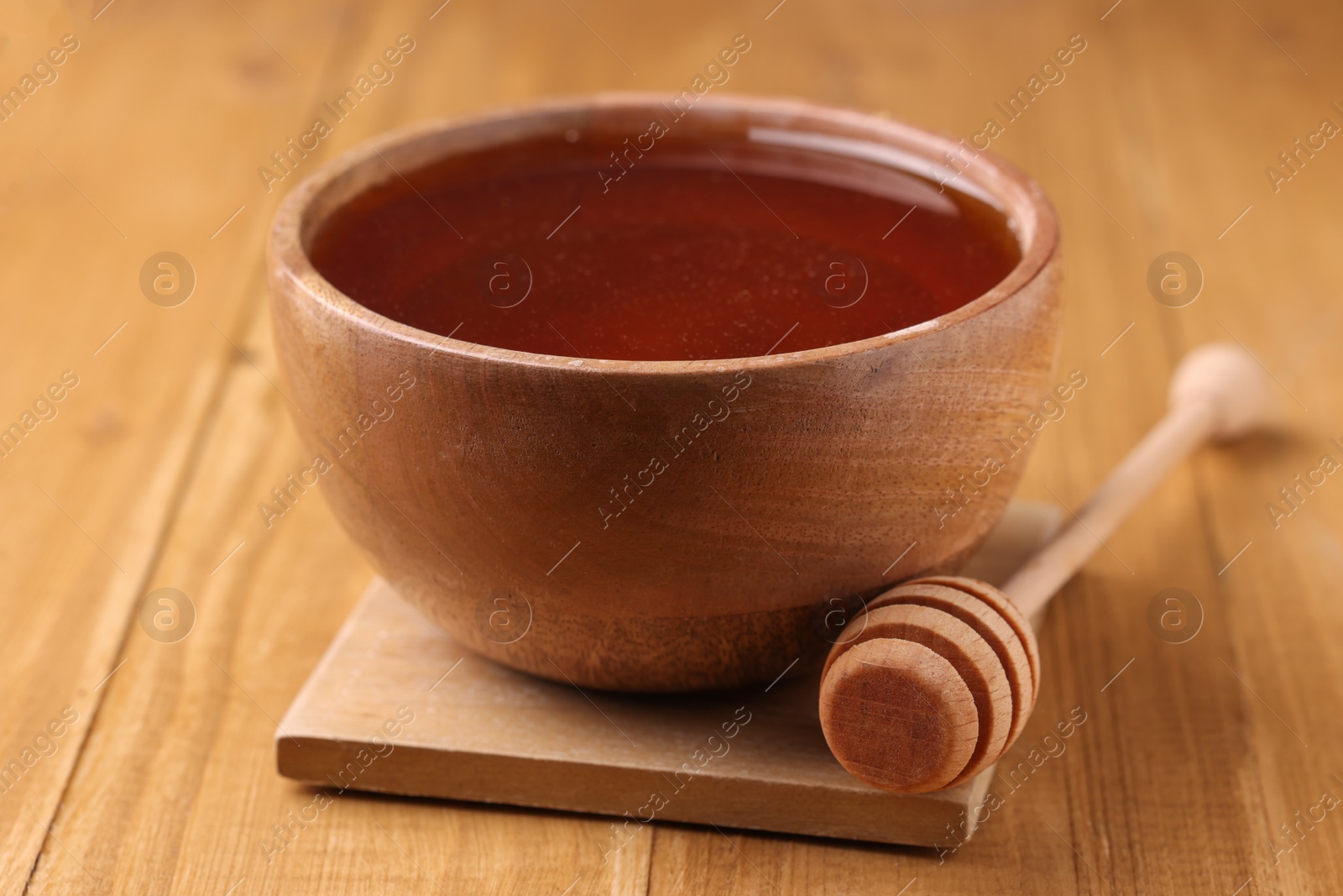 Photo of Delicious honey in bowl and dipper on wooden table, closeup