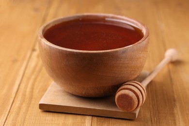 Delicious honey in bowl and dipper on wooden table, closeup