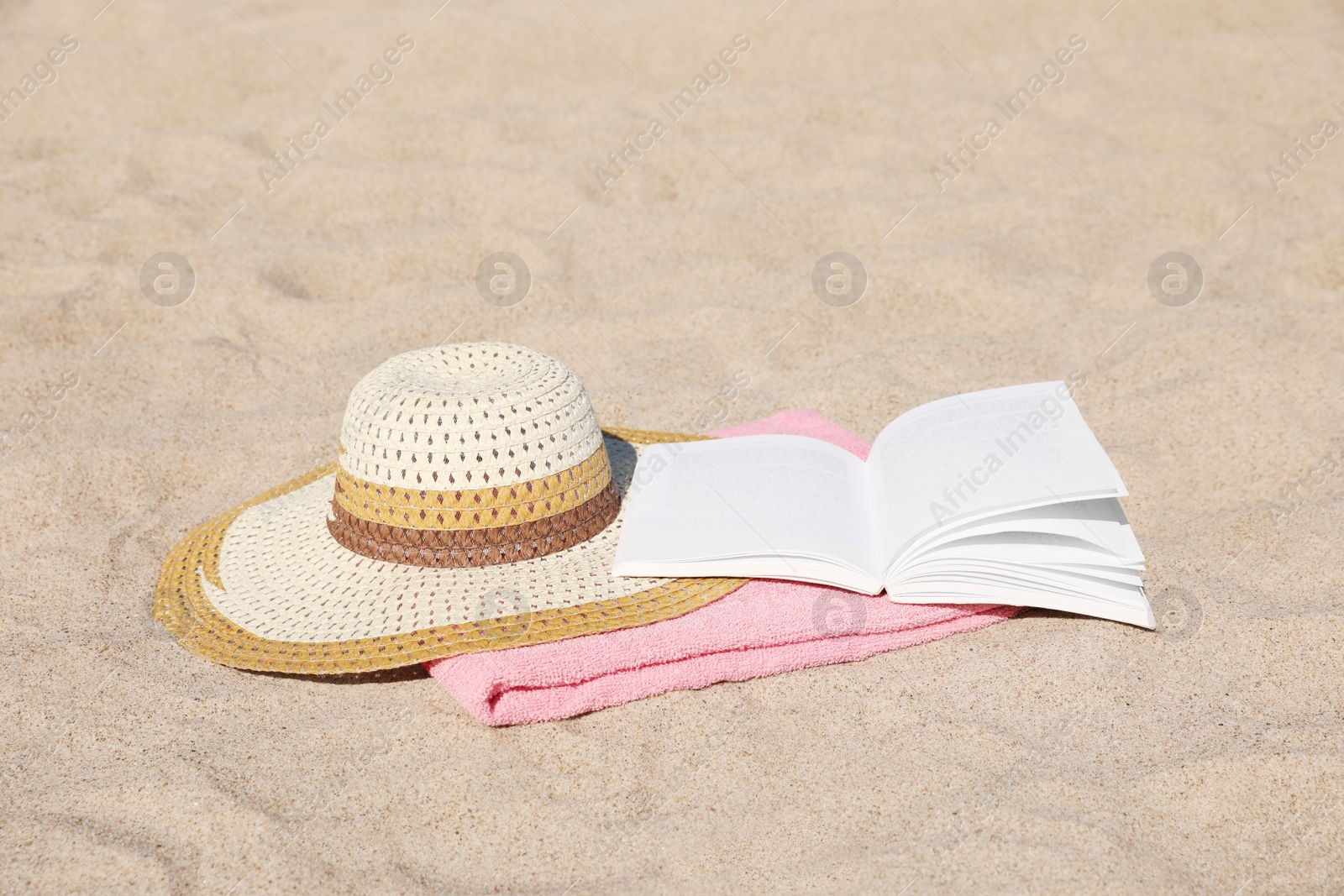 Photo of Open book, hat and pink towel on sandy beach