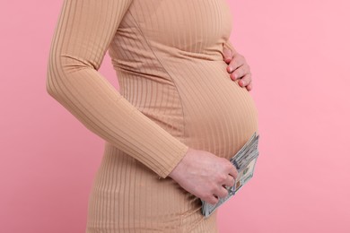 Photo of Surrogate mother. Pregnant woman with dollar banknotes on pink background, closeup