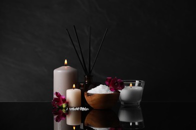 Photo of Beautiful spa composition with different care products and burning candles on mirror table against black background