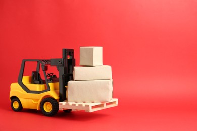 Photo of Toy forklift with wooden pallet and boxes on red background, space for text