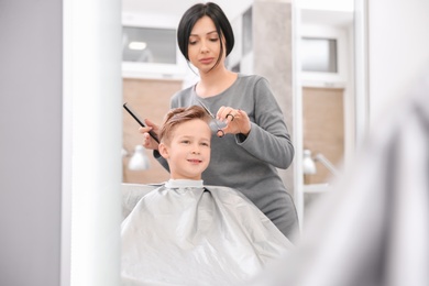 Photo of Professional female hairdresser working with little boy in salon