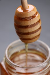 Photo of Pouring sweet honey from dipper into jar at table, closeup