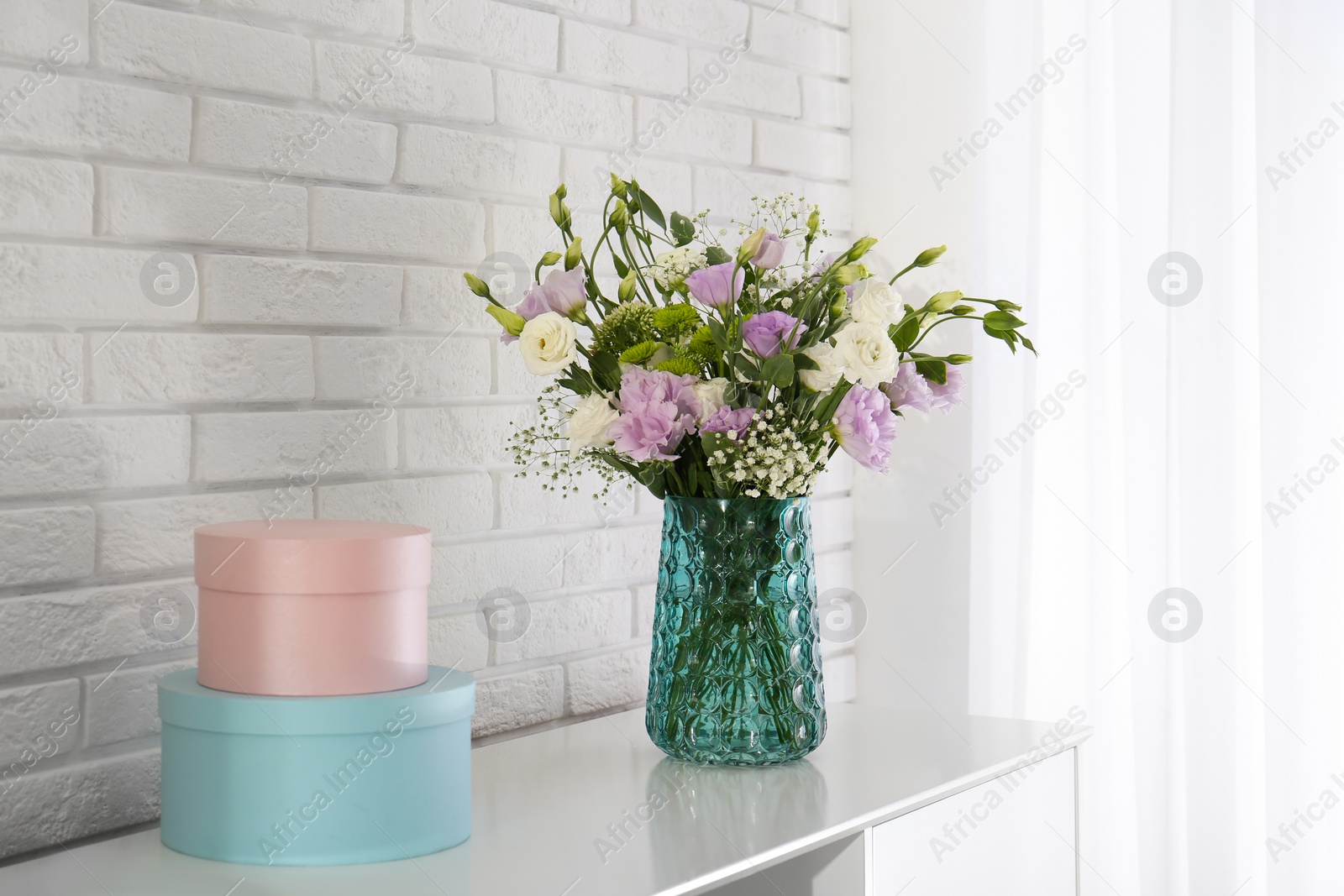 Photo of Bouquet of beautiful Eustoma flowers on cabinet near white brick wall