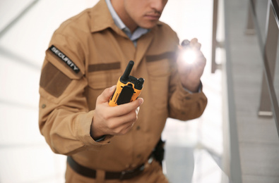 Photo of Professional security guard with portable radio set and flashlight indoors, closeup