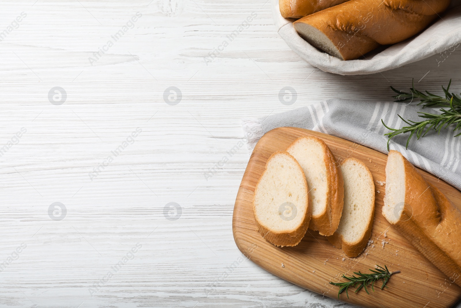 Photo of Cut tasty baguette with rosemary on white wooden table, flat lay. Space for text