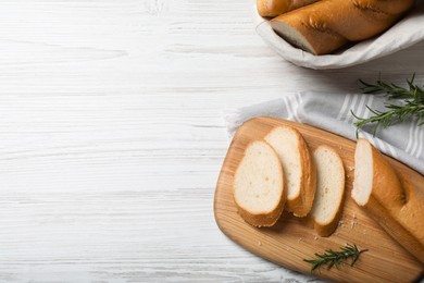 Photo of Cut tasty baguette with rosemary on white wooden table, flat lay. Space for text