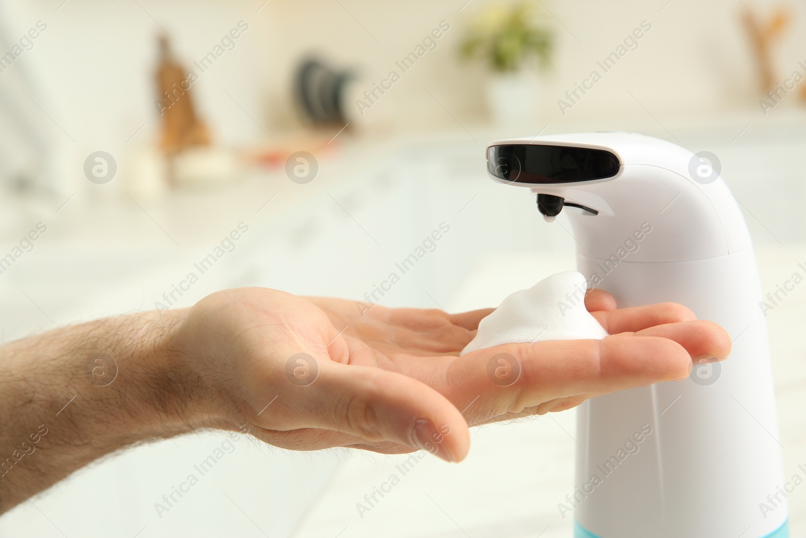 Photo of Man using automatic soap dispenser in kitchen, closeup