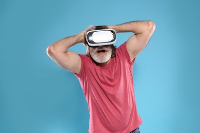 Emotional mature man playing video games with virtual reality headset on color background