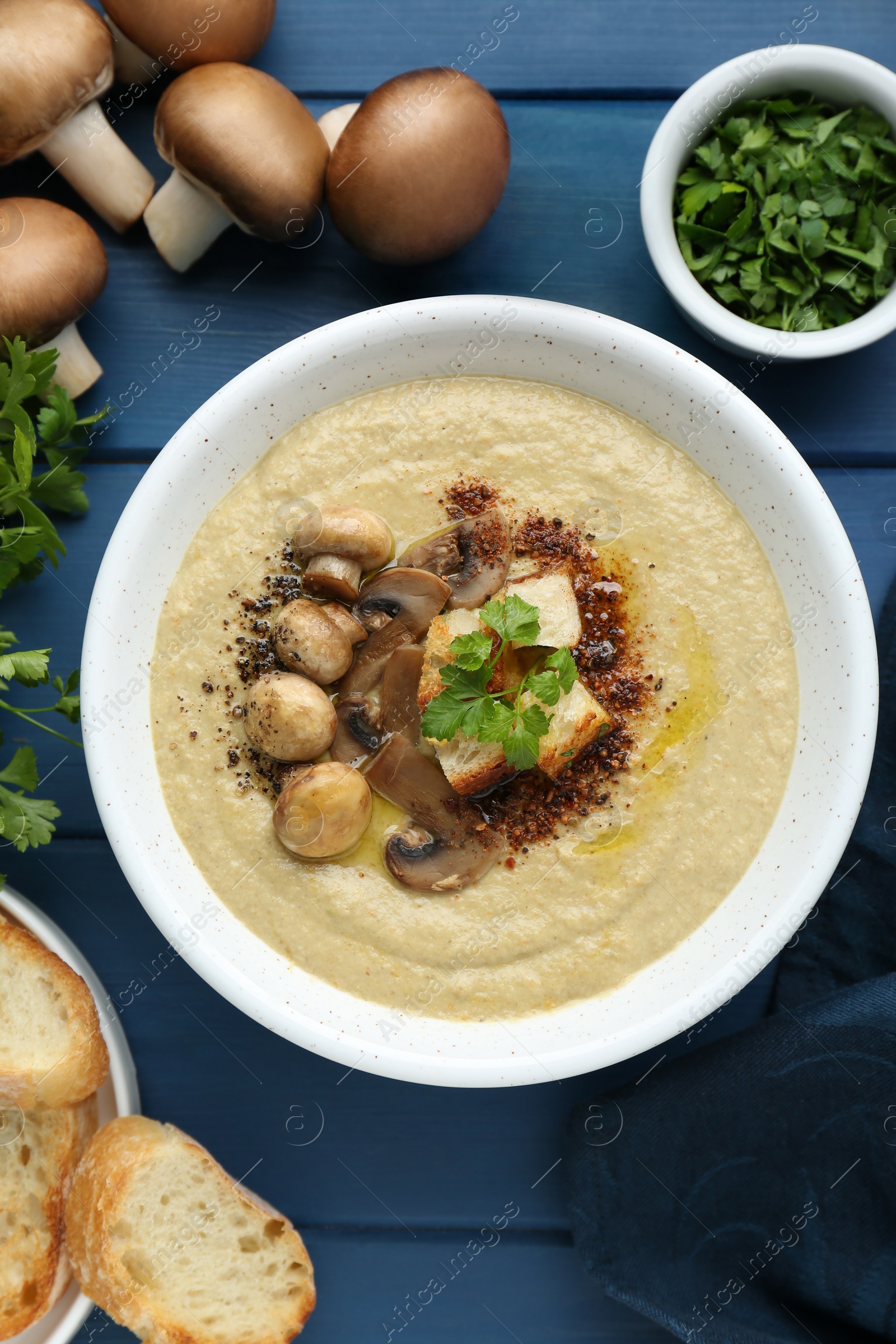 Photo of Delicious mushroom cream soup and ingredients on blue wooden table, flat lay