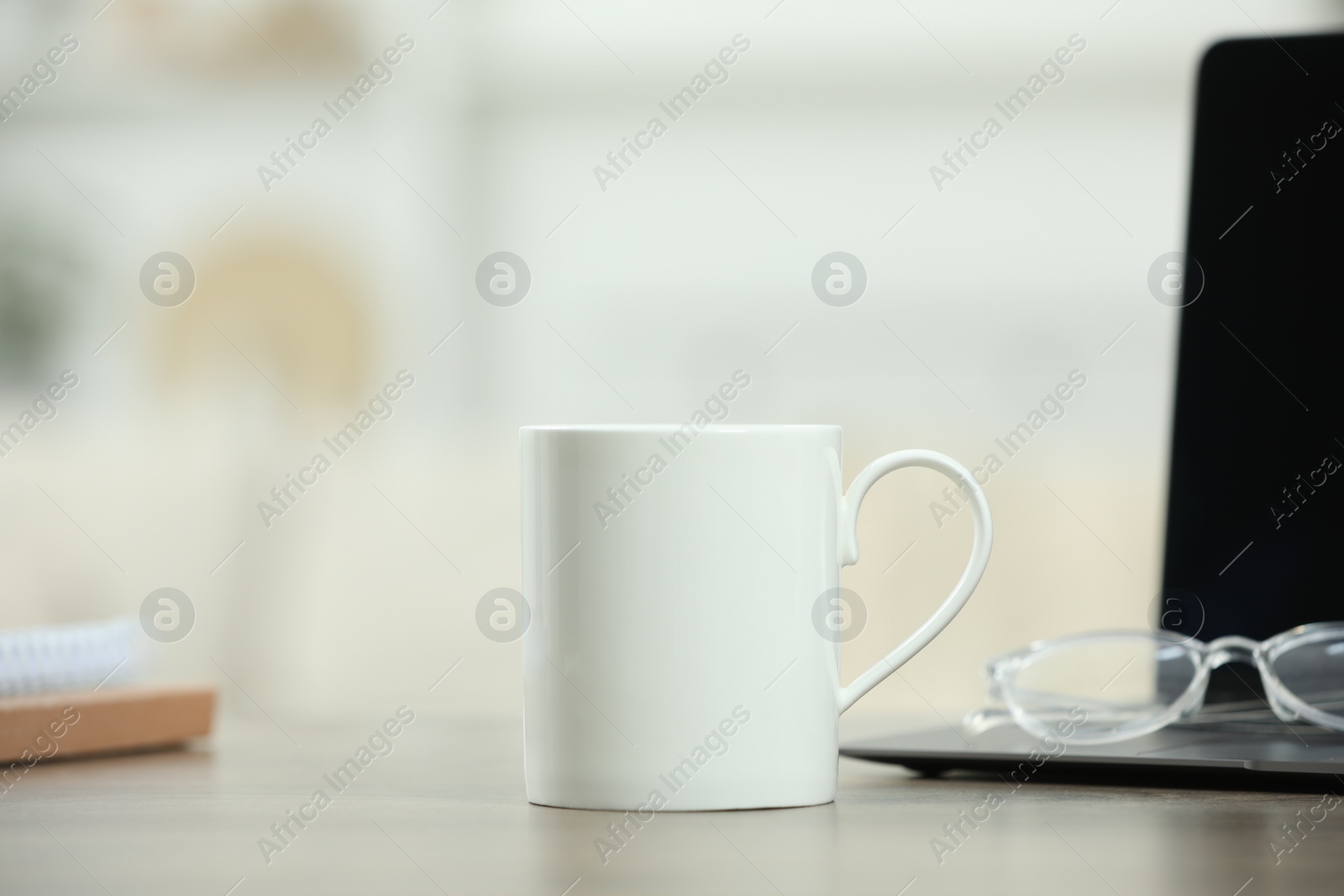 Photo of White ceramic mug, glasses and laptop on wooden table indoors. Space for text