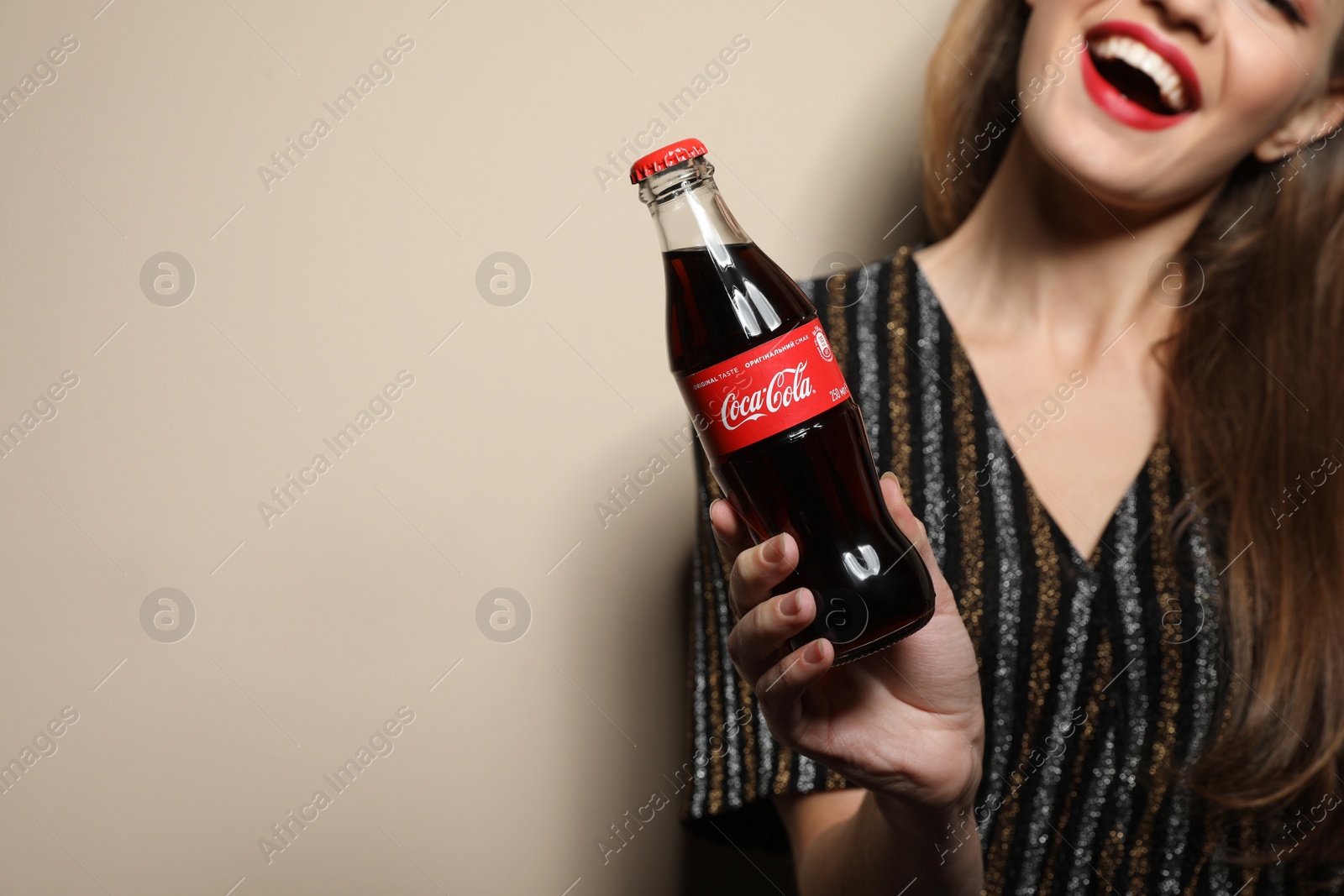 Photo of MYKOLAIV, UKRAINE - NOVEMBER 28, 2018: Young woman with bottle of Coca-Cola on color background, closeup. Space for text