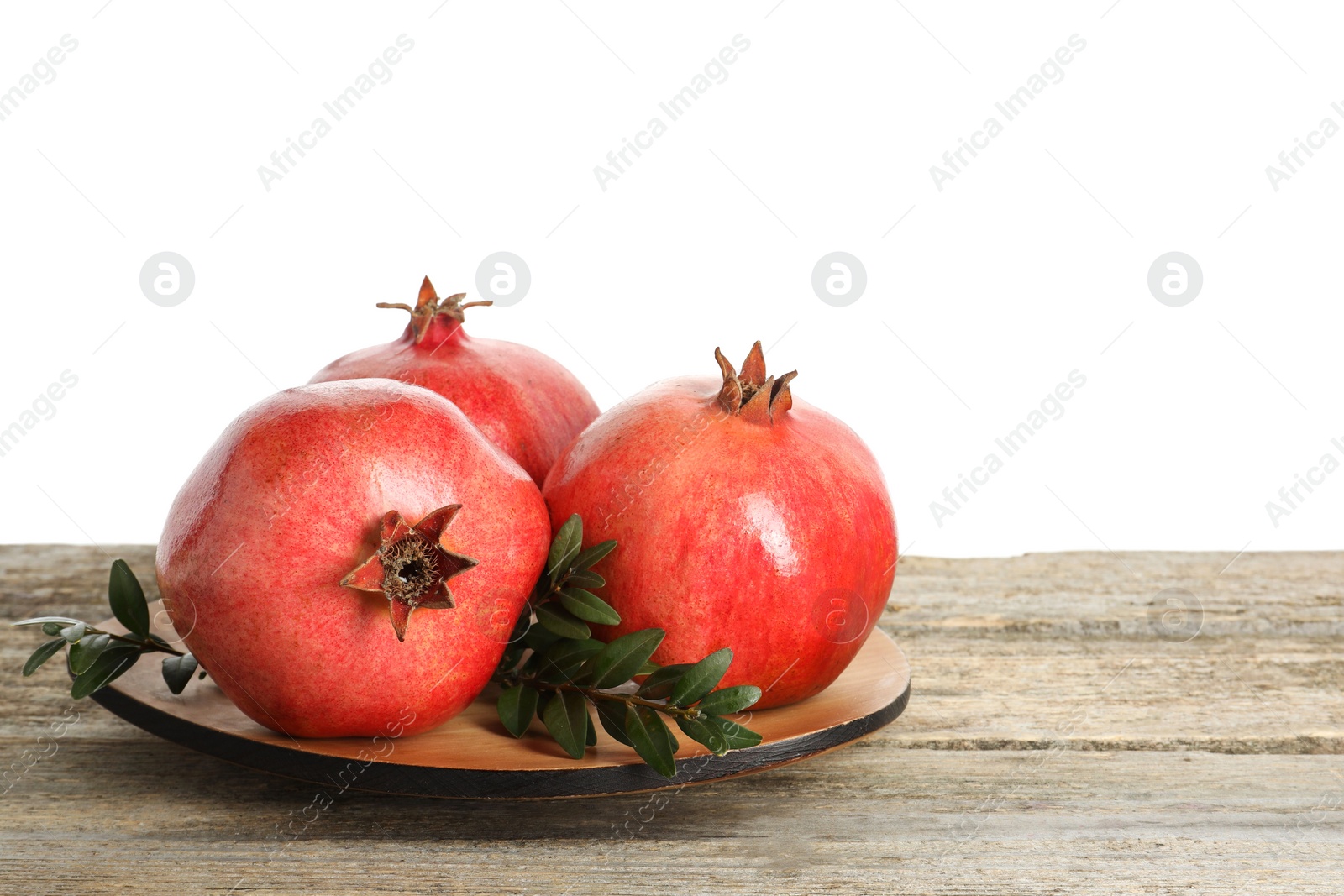 Photo of Fresh pomegranates and green leaves on wooden table against white background