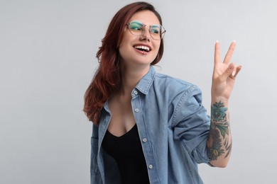 Photo of Beautiful tattooed woman showing V-sign on gray background