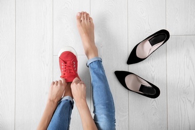 Young woman changing shoes on wooden background, top view