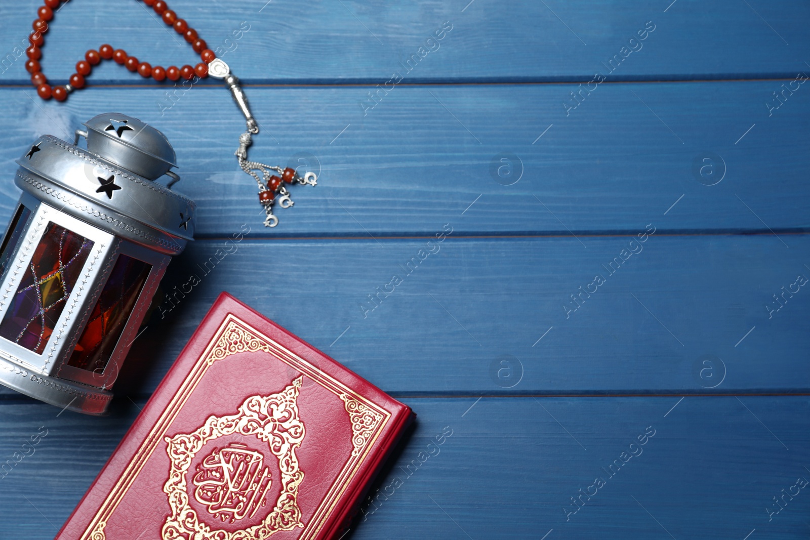 Photo of Arabic lantern, quran and misbaha on blue wooden table, flat lay. Space for text