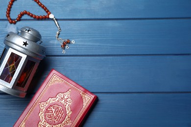 Photo of Arabic lantern, quran and misbaha on blue wooden table, flat lay. Space for text
