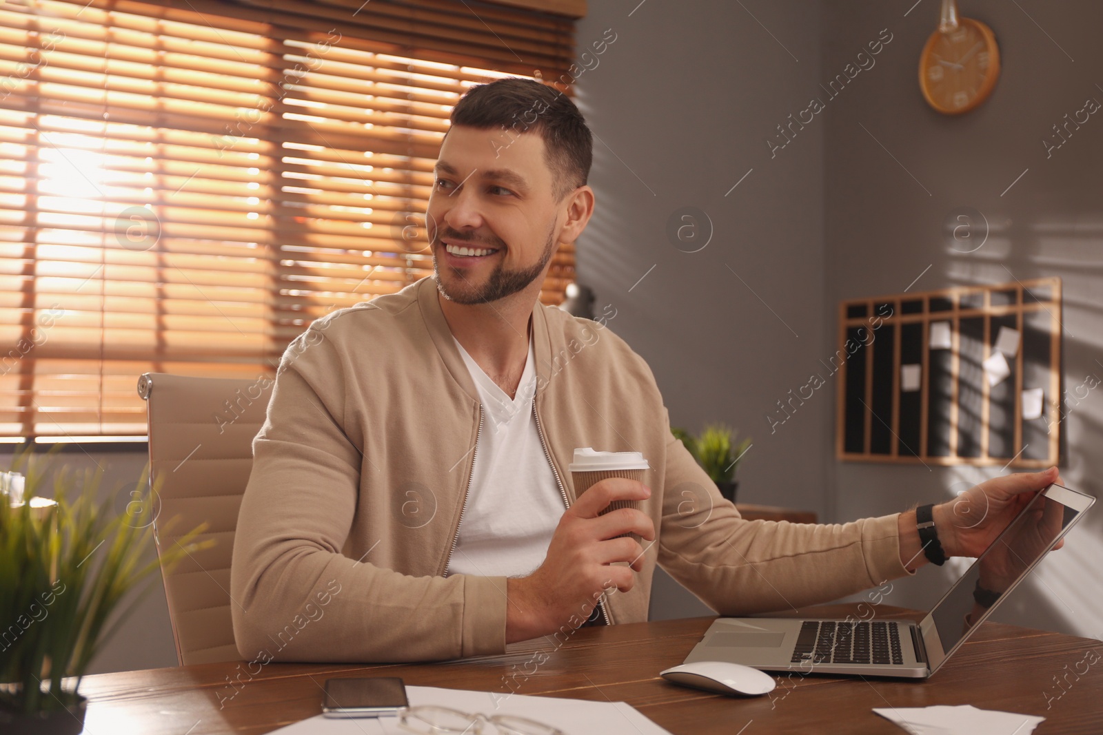 Photo of Freelancer with cup of coffee working on laptop at table indoors