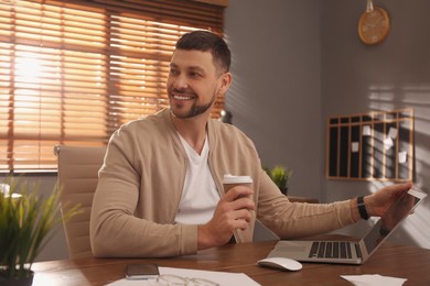 Photo of Freelancer with cup of coffee working on laptop at table indoors