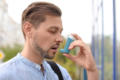 Photo of Man using asthma inhaler outdoors. Health care