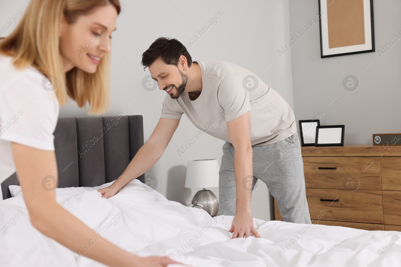 Photo of Couple changing bed linens in room. Domestic chores