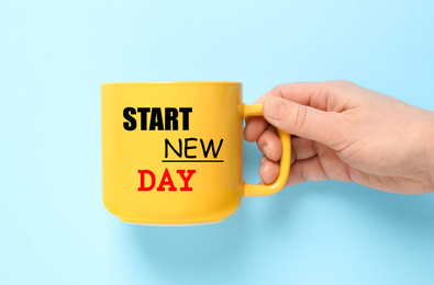 Woman holding cup with words START NEW DAY on light blue background, closeup