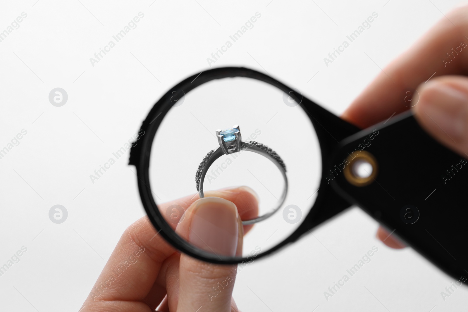 Photo of Jeweler examining topaz ring with magnifying glass on white background, closeup