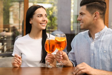 Photo of Happy couple clinking glasses of Aperol spritz cocktails outdoors