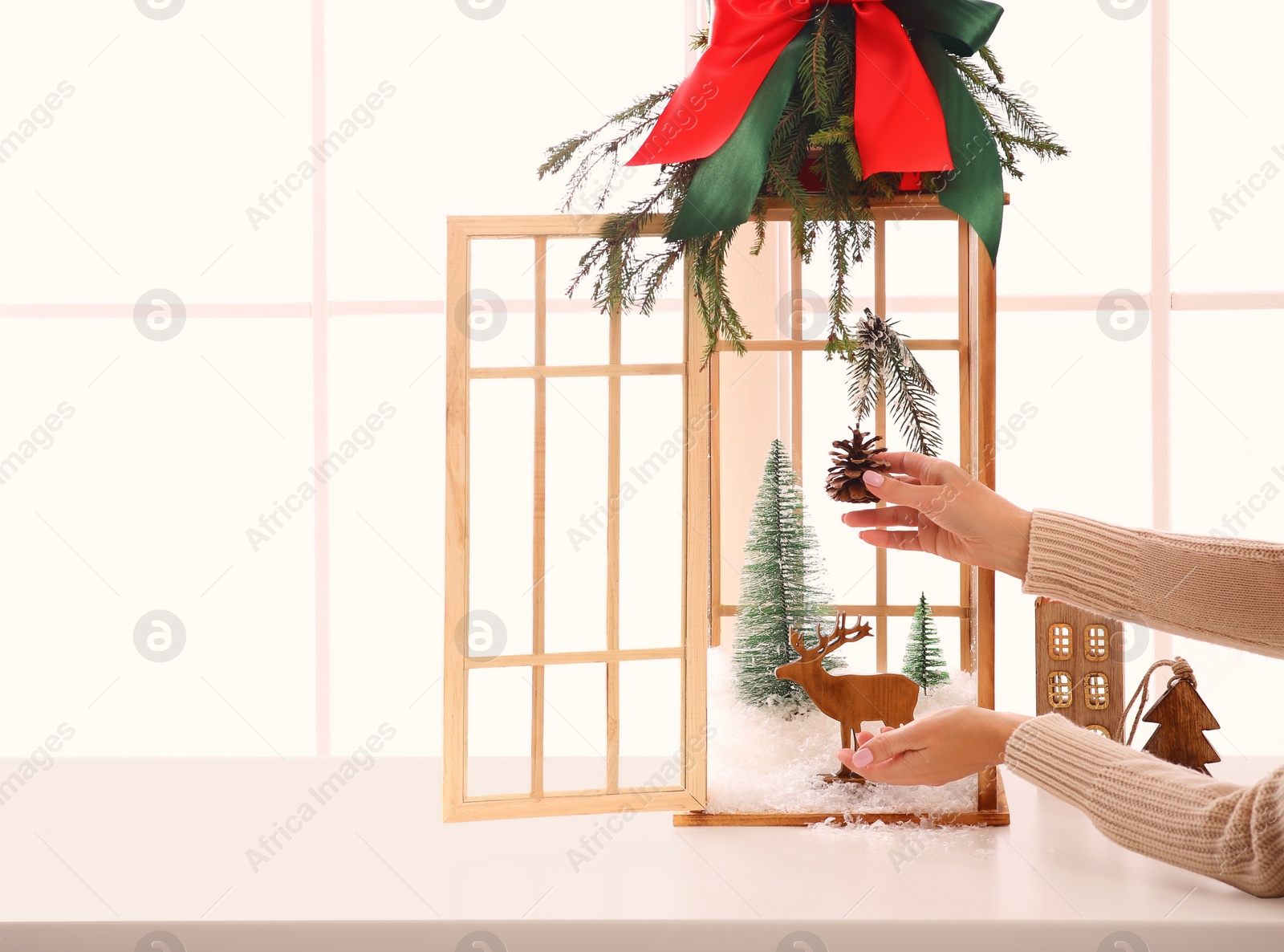Photo of Woman creating Christmas composition inside of vintage wooden lantern on window sill indoors, closeup. Space for text