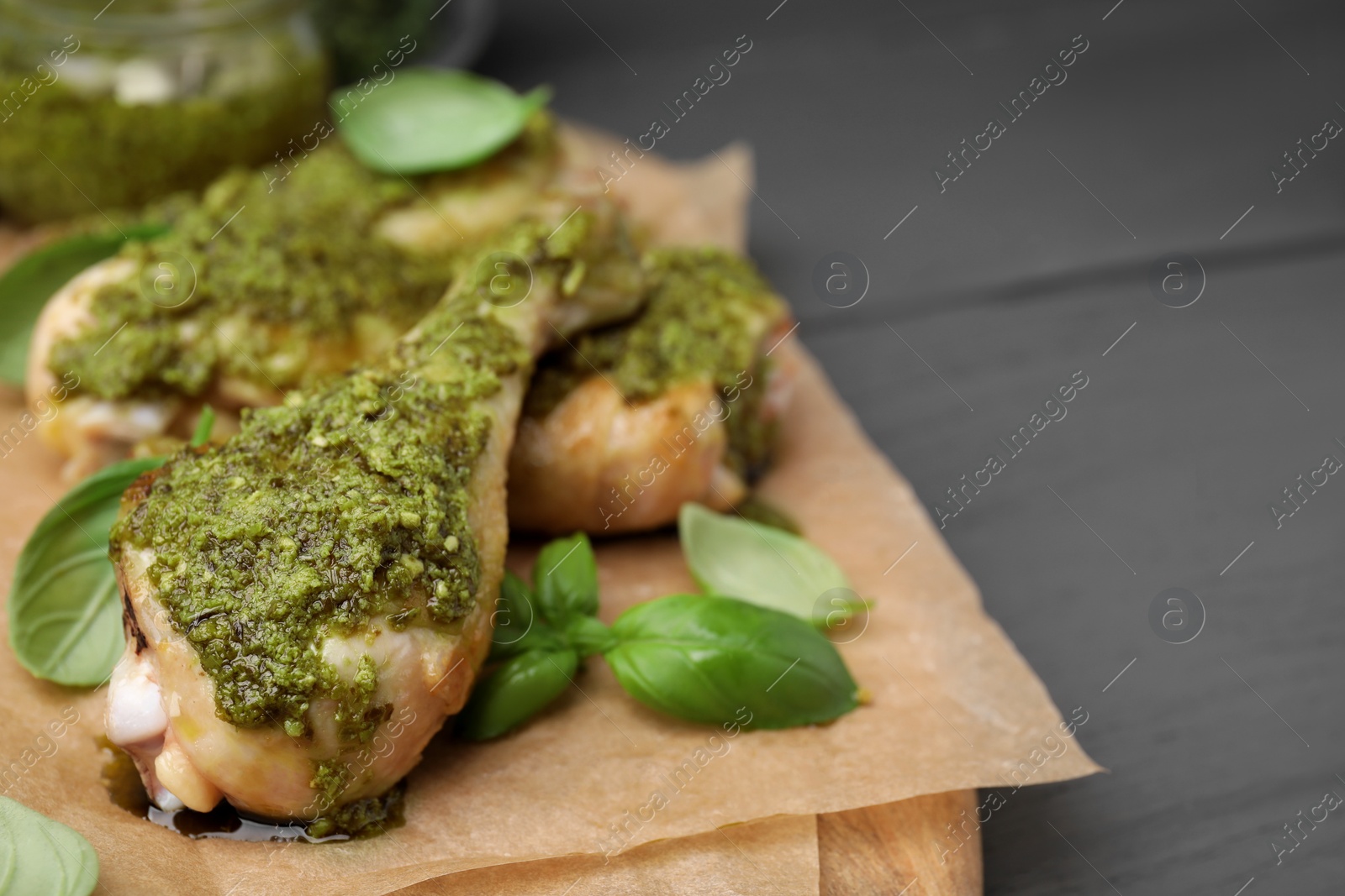 Photo of Delicious fried chicken drumsticks with pesto sauce and basil on gray table, closeup. Space for text