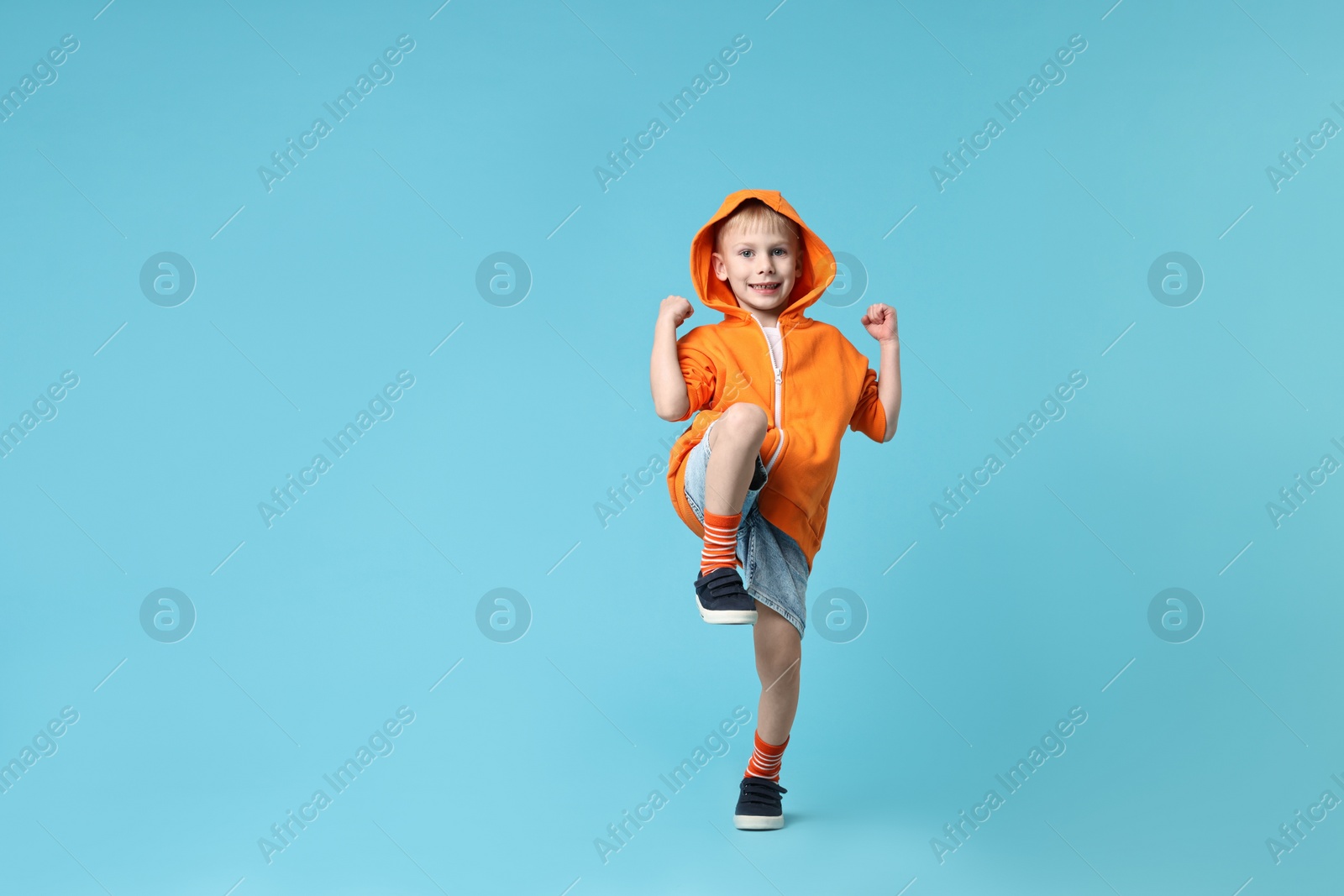 Photo of Happy little boy dancing on light blue background. Space for text