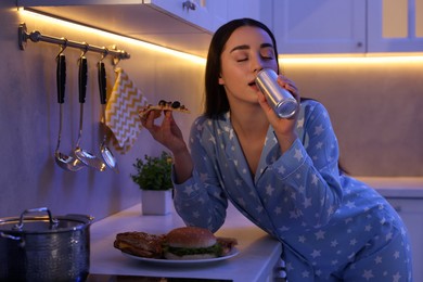 Photo of Young woman eating junk food in kitchen at night. Bad habit