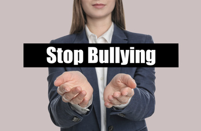 Young woman showing sign STOP BULLYING on light background, closeup