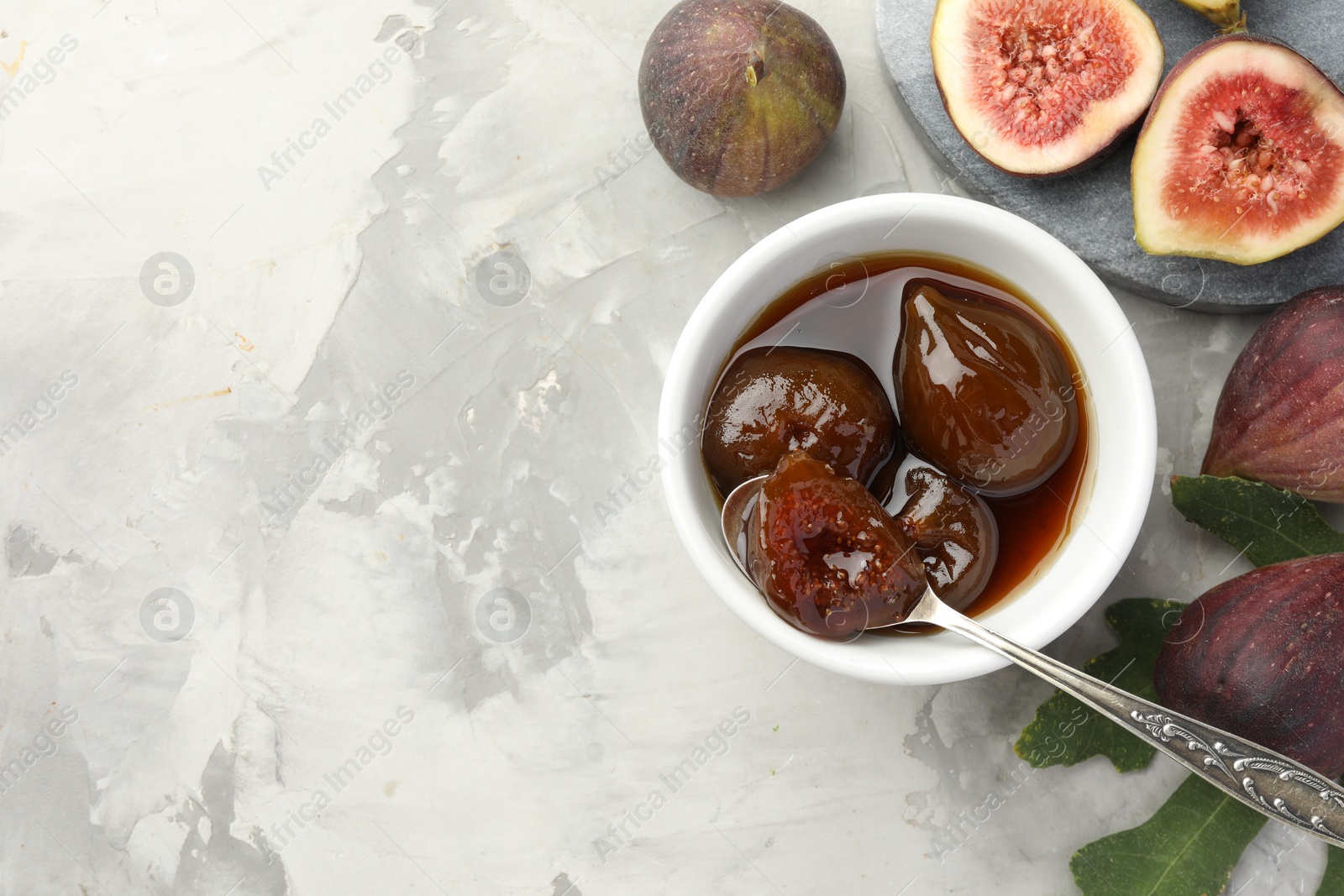 Photo of Bowl of tasty sweet jam and fresh figs on grey table, flat lay. Space for text