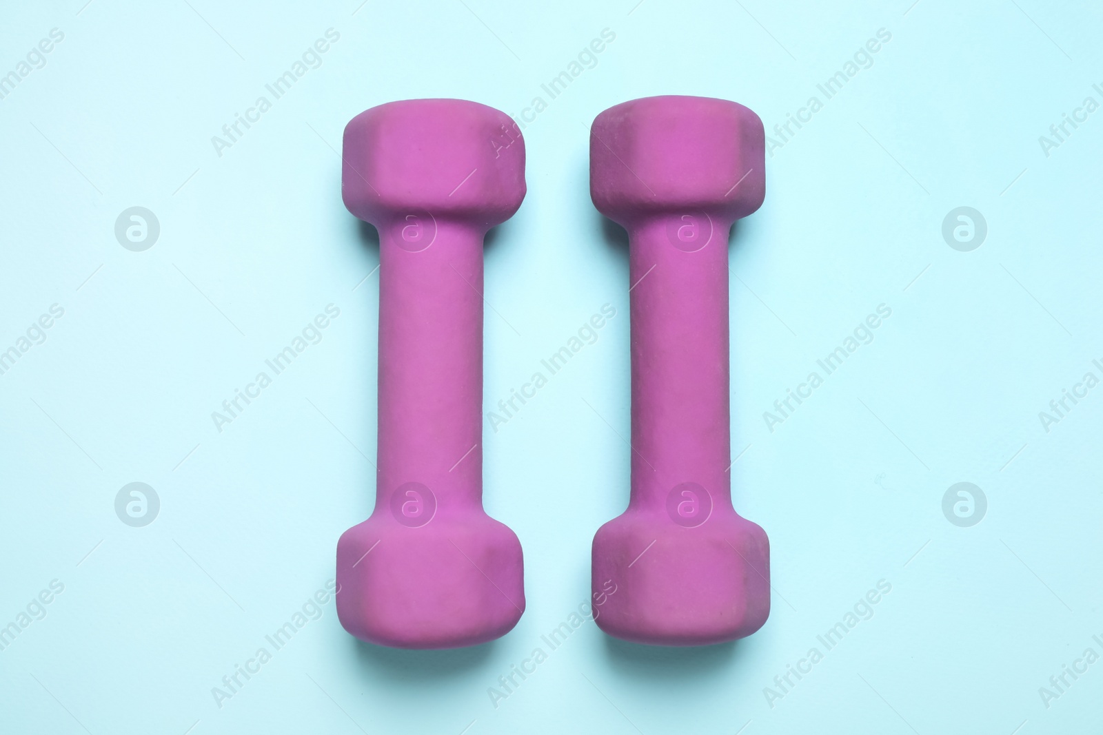 Photo of Bright dumbbells on light blue background, flat lay