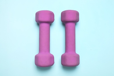 Photo of Bright dumbbells on light blue background, flat lay