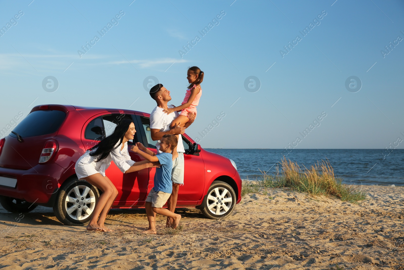 Photo of Happy family having fun near car on sandy beach. Summer trip